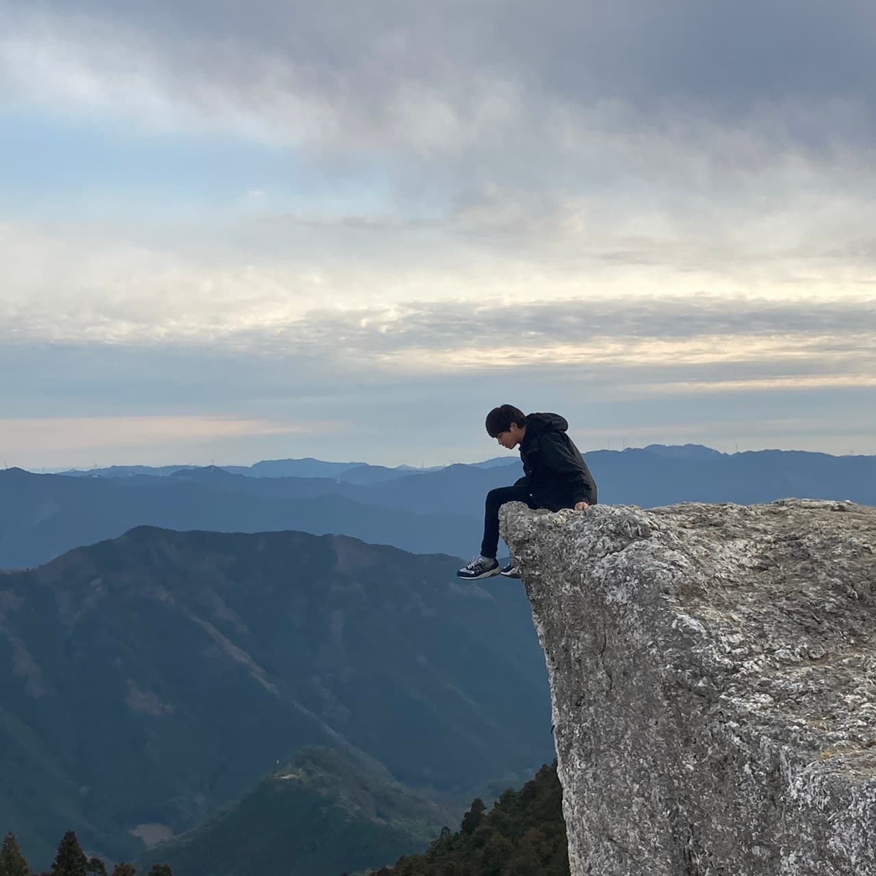 Shota Kawamura, founder of Wander Japan, sitting on a rock outcrop overlooking mountains in Japan